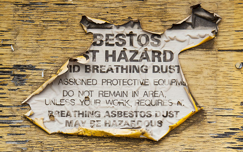 Torn hazard sign on pealing yellow painted wall